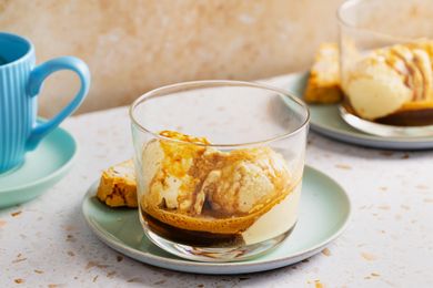 A serving of affogato with ice cream submerged in espresso served with biscotti on a light plate