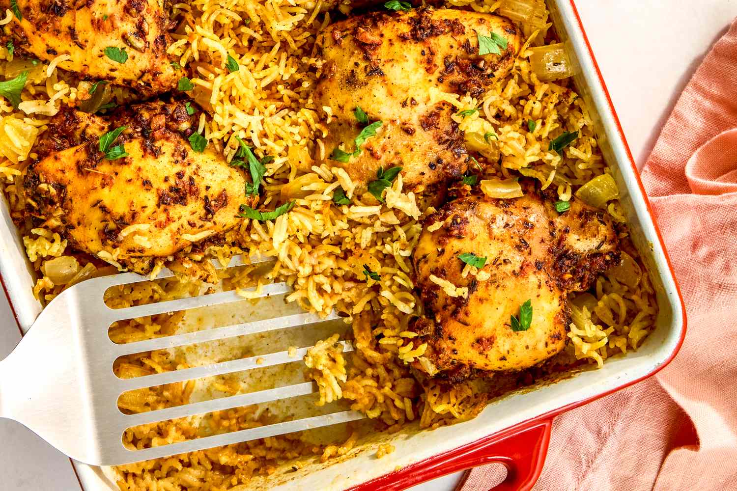 Baked chicken and rice dish in a casserole with a serving spatula placed nearby