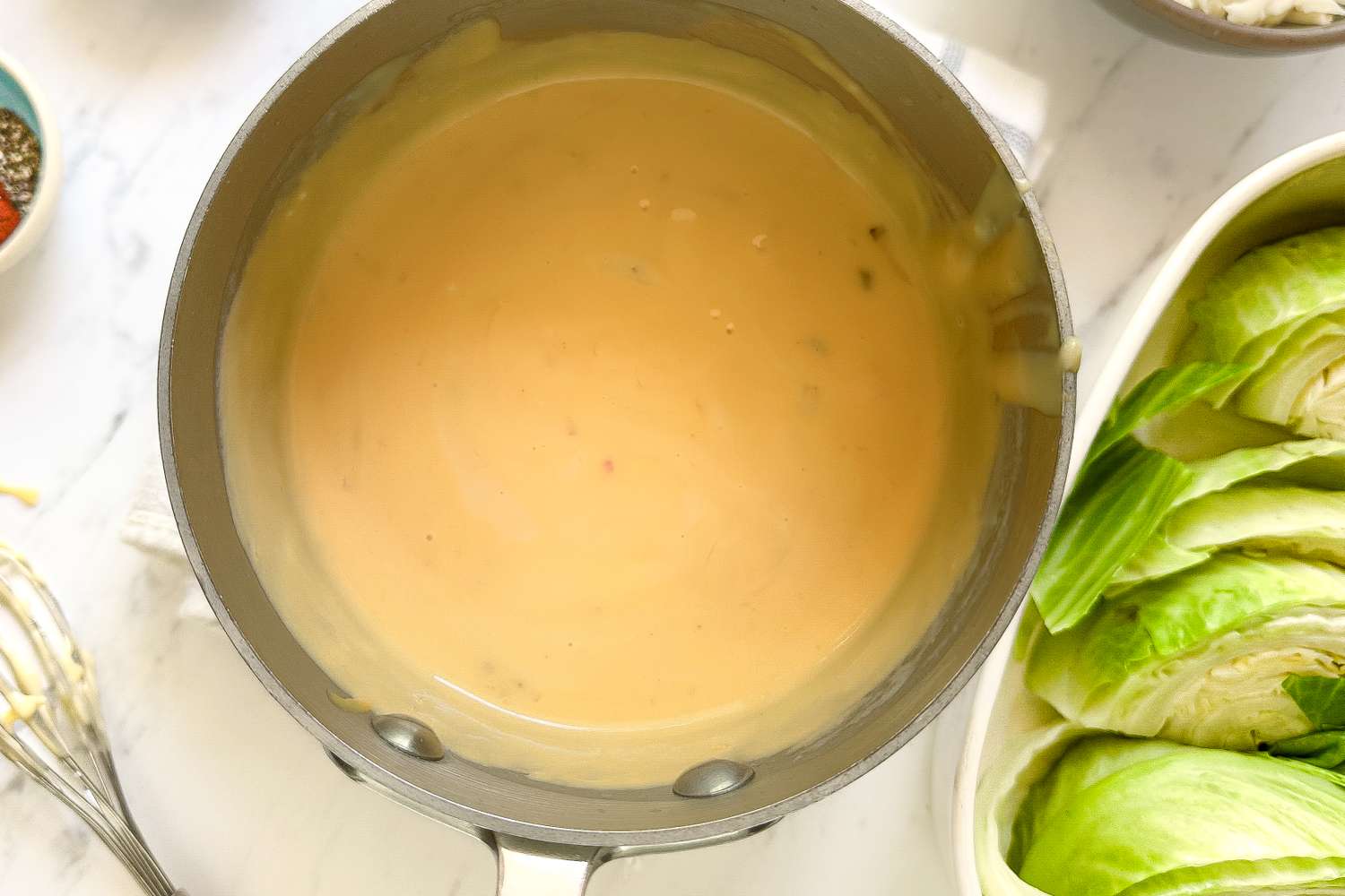 A saucepan containing a creamy sauce next to halved cabbages