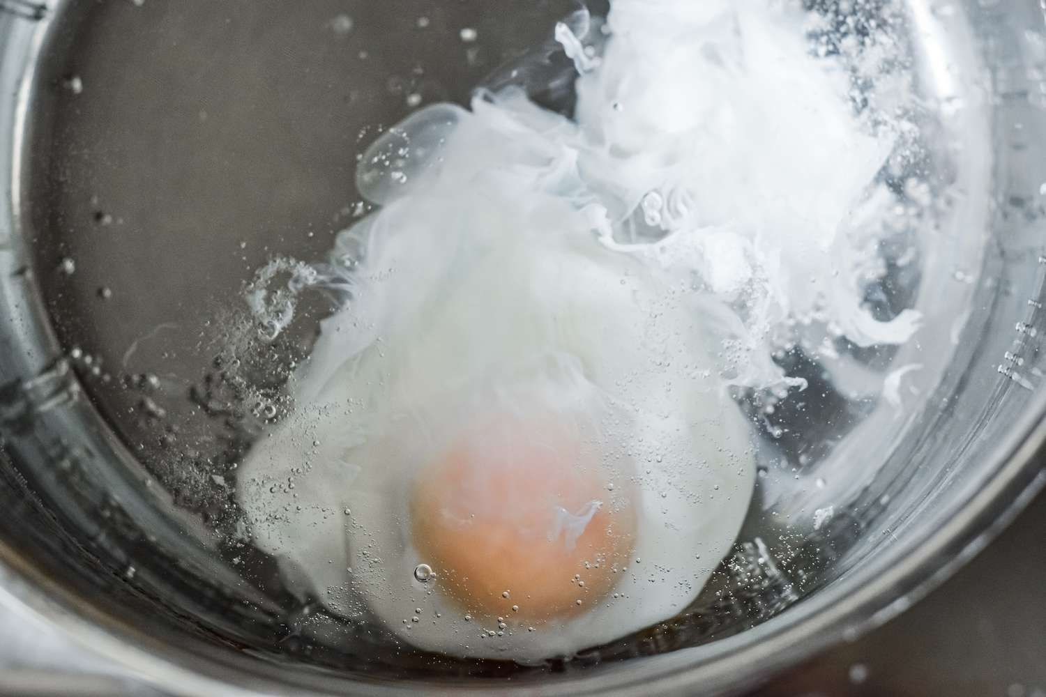Cracked egg added to simmering water for a poached egg recipe.