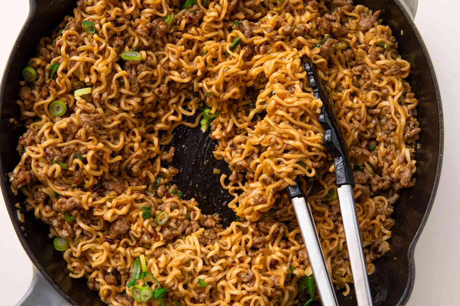 Overhead view of a cast iron skillet of pork and garlic noodles with tongs