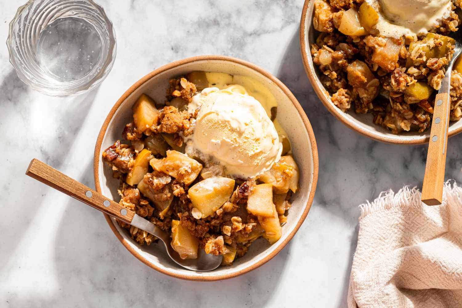Two bowls of apple crisp dessert with ice cream served with wooden spoons