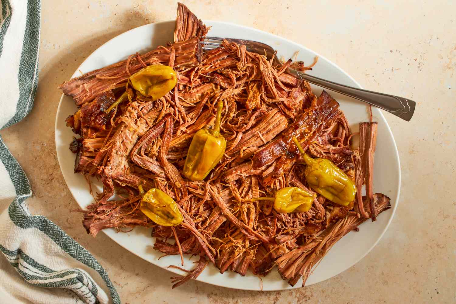 Shredded roast beef with peppers on a white plate with a fork served on a beige table