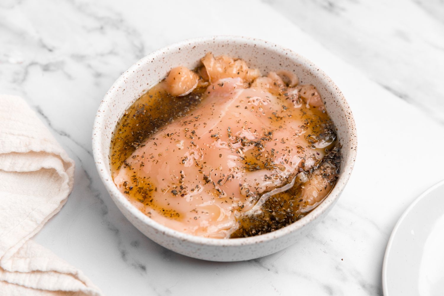 Sliced Chicken Marinating in a Bowl Next to a White Kitchen Towel