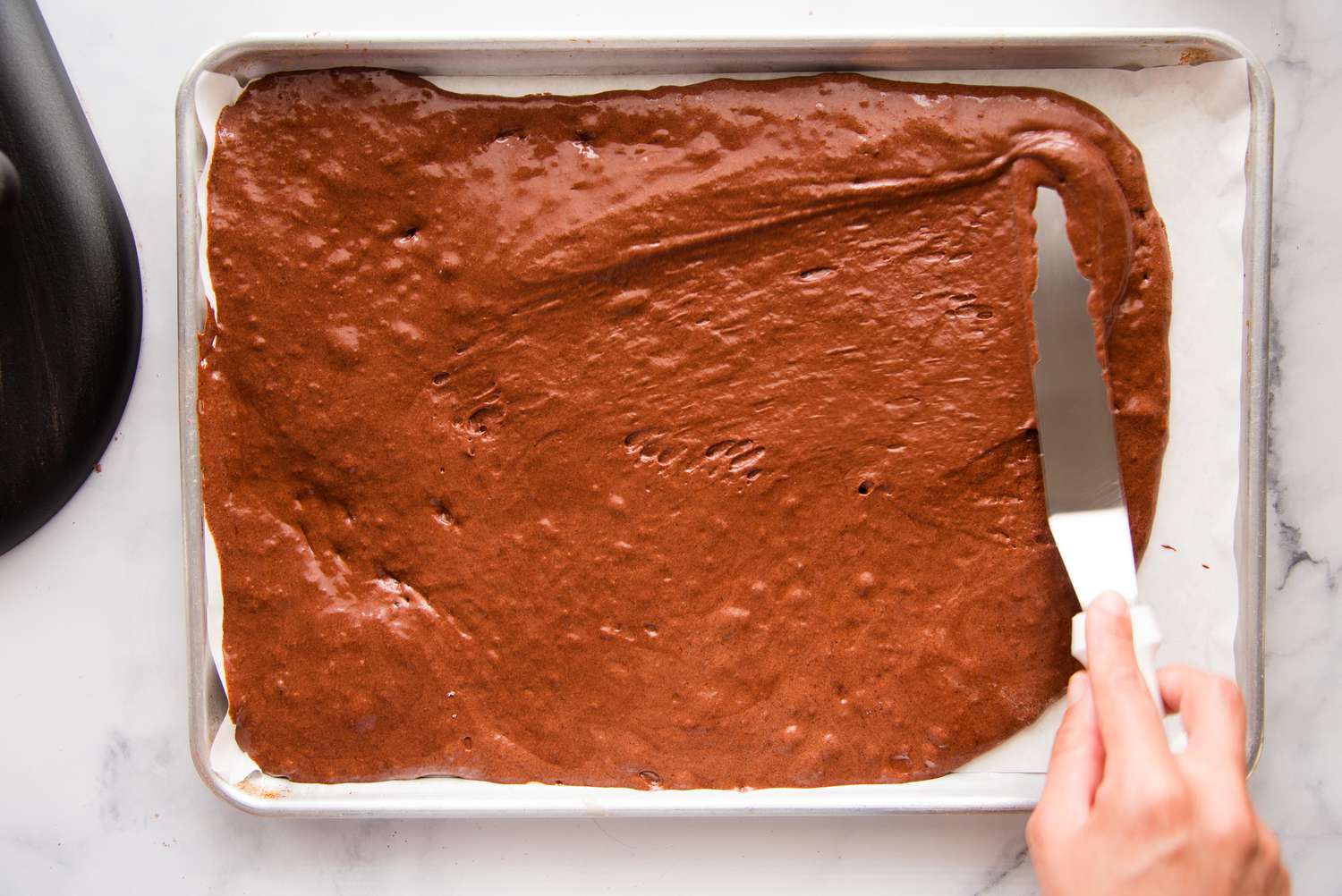Spreading chocolate batter on a baking sheet with a offset spatula.