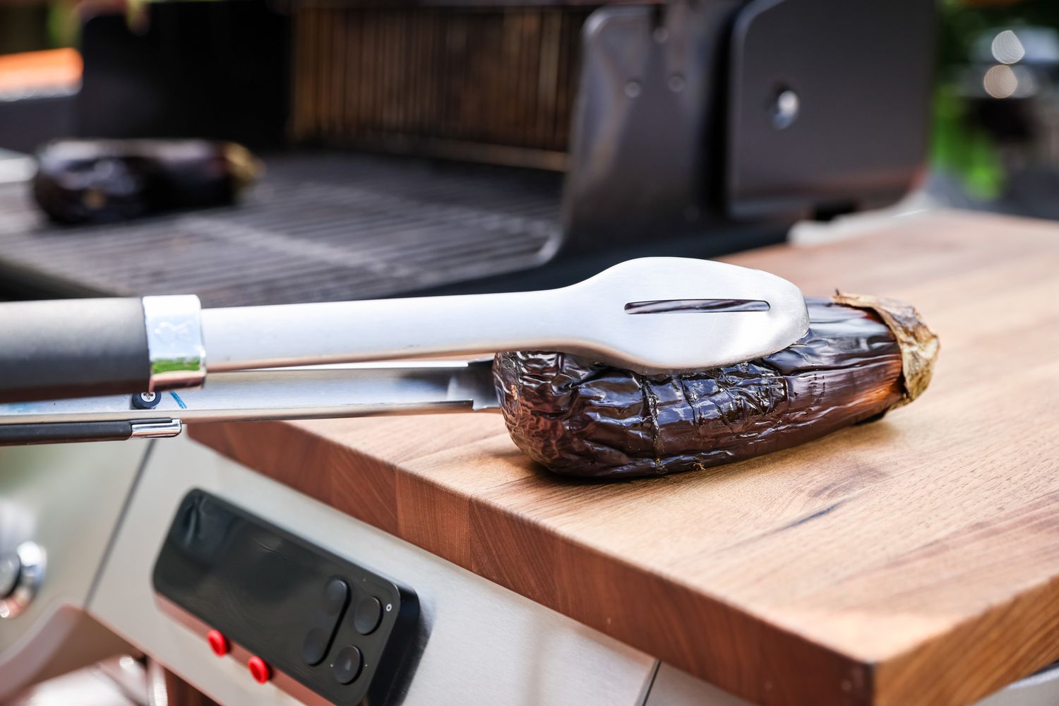 Whole Grilled Eggplant Placed on Cutting Board Using Tongs