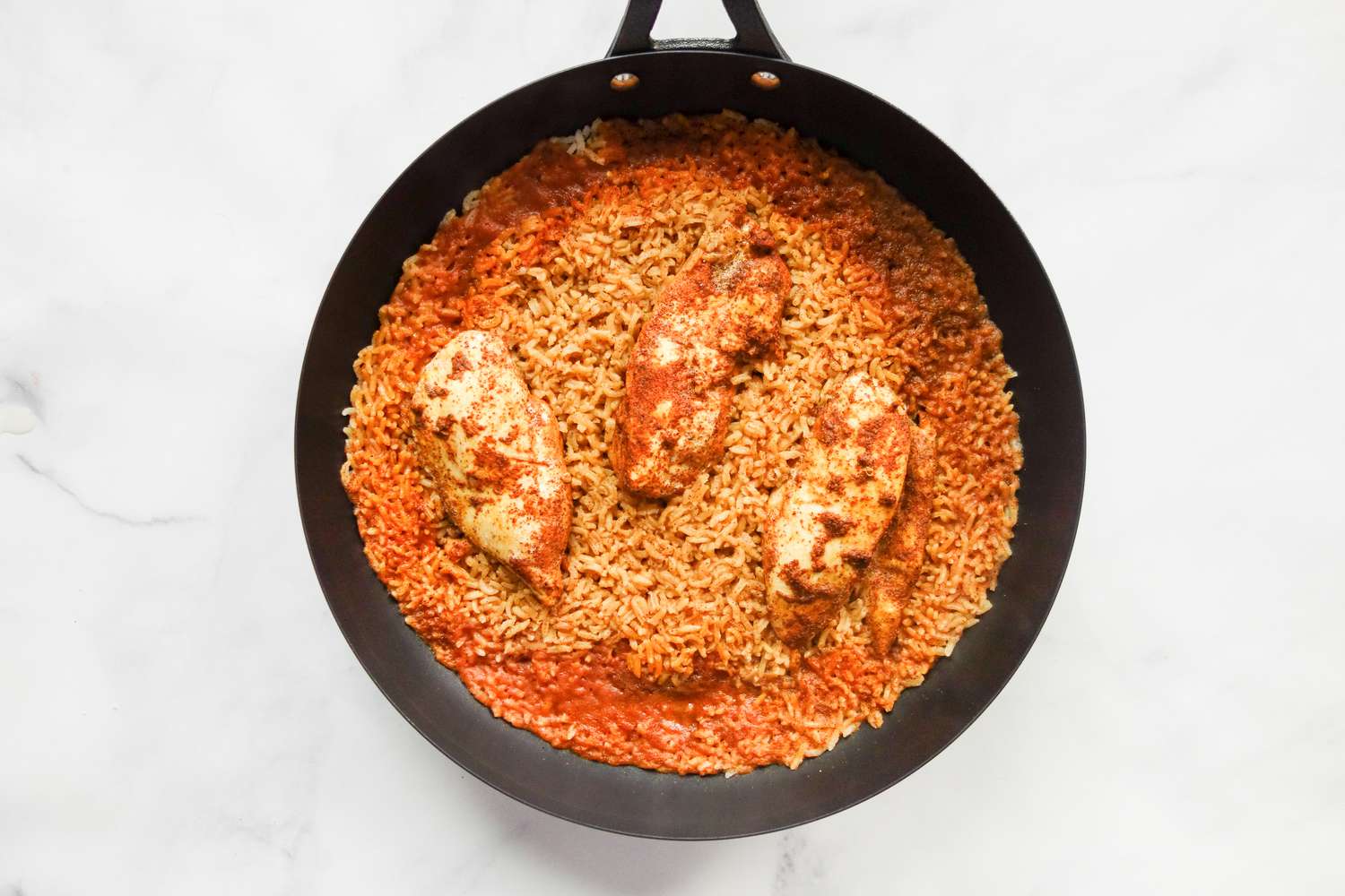 Cooked chicken on top of rice in skillet.