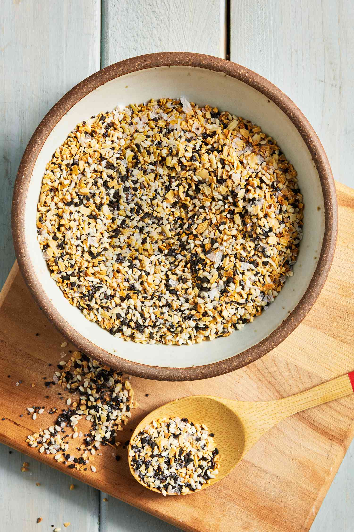 On a Wooden Board, a Bowl of Everything Bagel Seasoning, a Wooden Spoon With Some Seasoning in It, and More Seasoning on the Board
