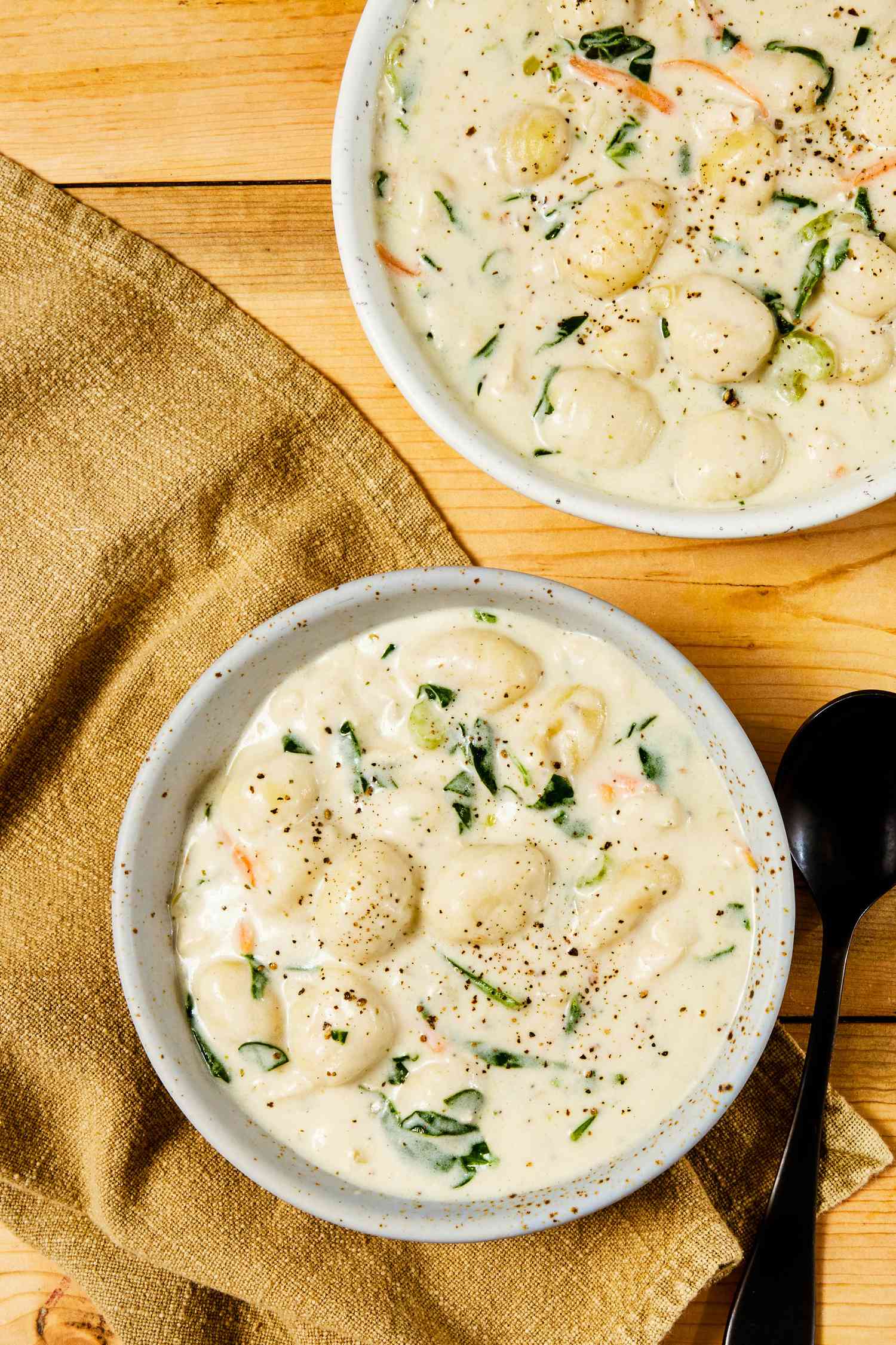 Overhead shot: two bowls of copycat Olive Garden chicken and gnocchi soup on a beige table napkin