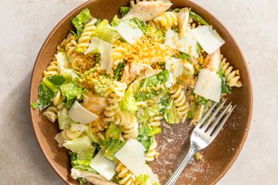 A bowl of pasta salad with chicken and shredded cheese on top, fork on the side