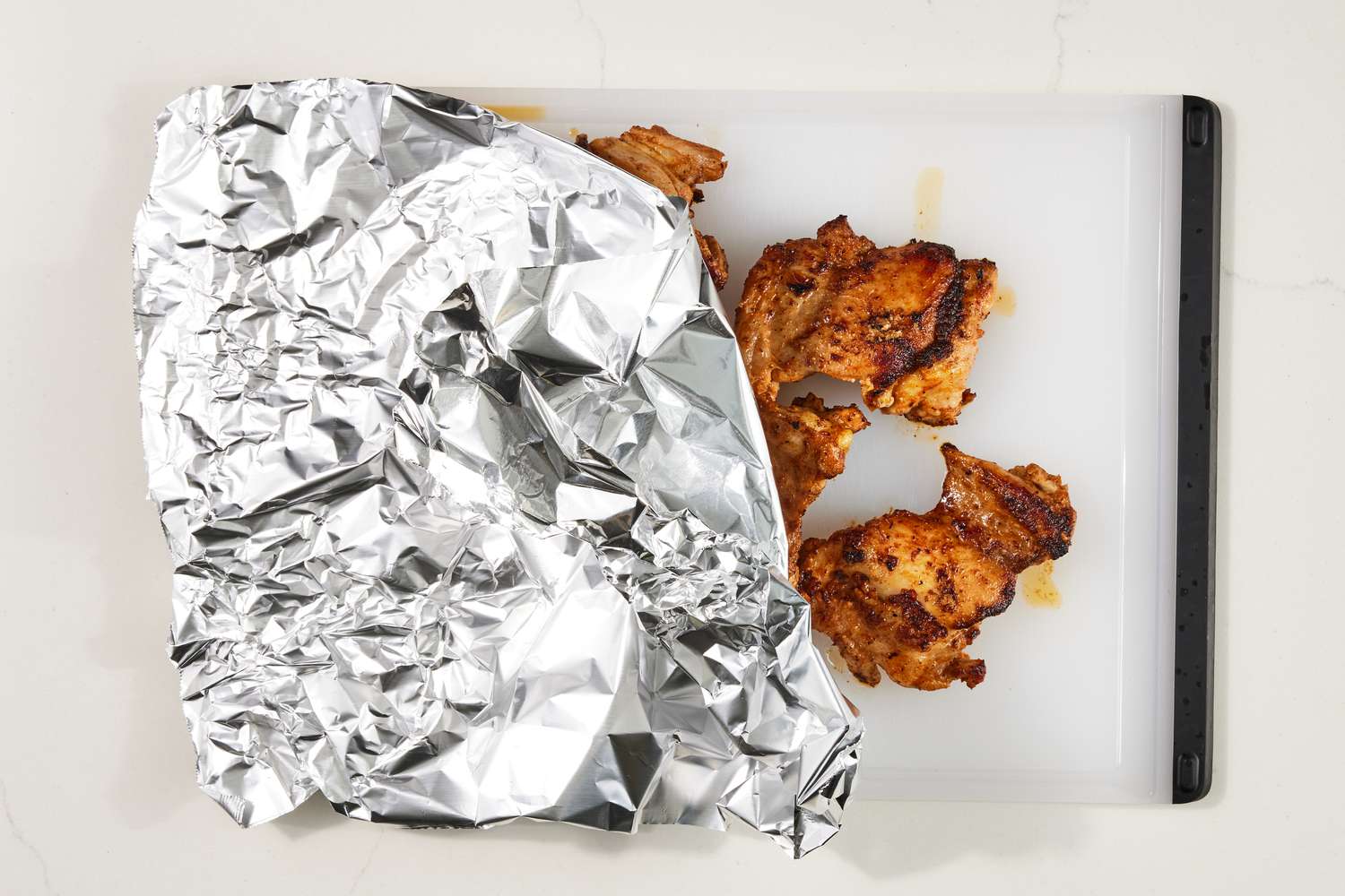 Copycat Chipotle chicken covered in aluminum foil and resting on a cutting board