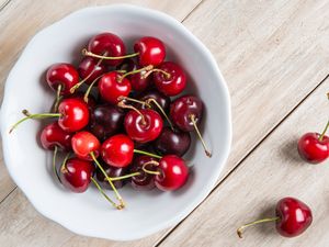 White bowl of fresh cherries on a wooden table