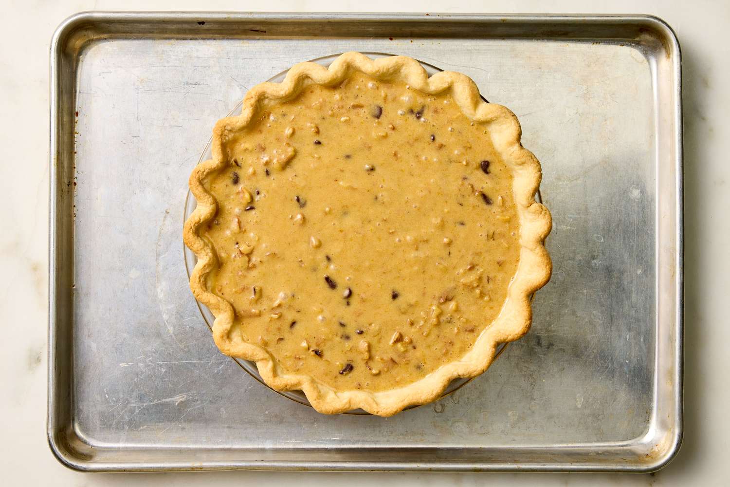 pie dough with filling added in a pie plate on top of a sheet pan