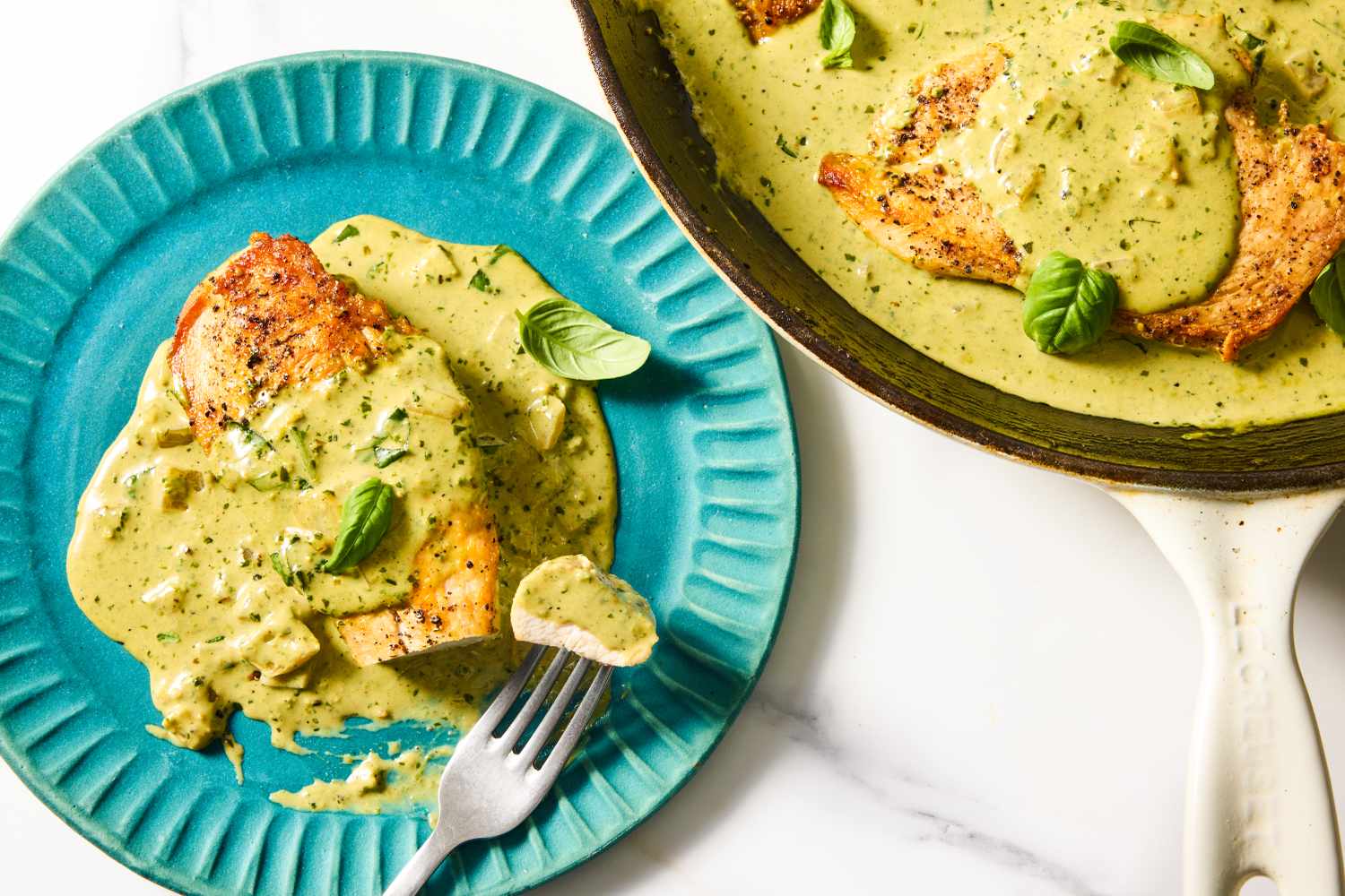 Chicken breast with pesto sauce on a plate alongside a skillet