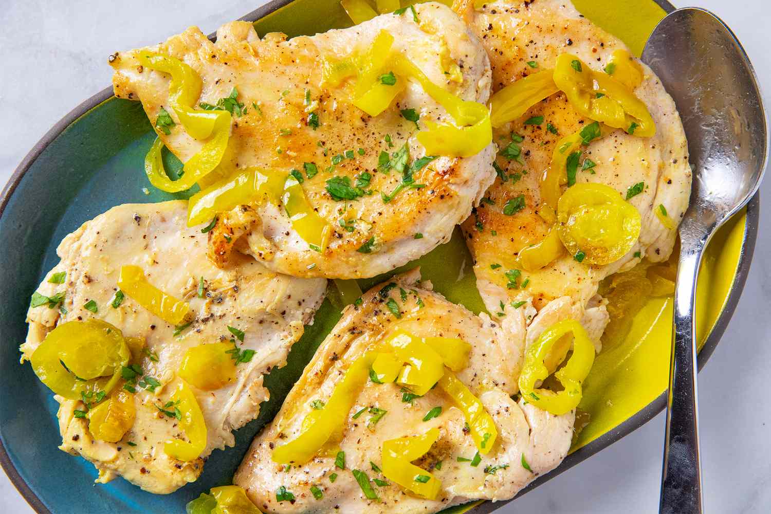Cooked chicken breasts topped with banana pepper slices on a serving plate with a spoon