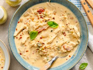 A bowl of creamy Marry Me Chicken Chili garnished with herbs and spices with a spoon resting inside