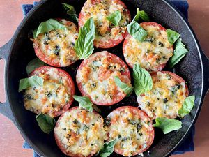 Overhead view of a cast iron skillet with vegetarian stuffed tomatoes with basil leaves scattered over top.