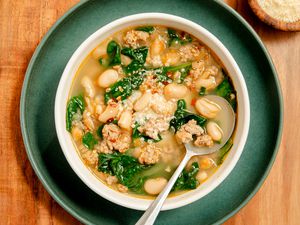 serving of 15-Minute Sausage White Bean Soup in a white bowl on a dark green plate on a wooden serving board