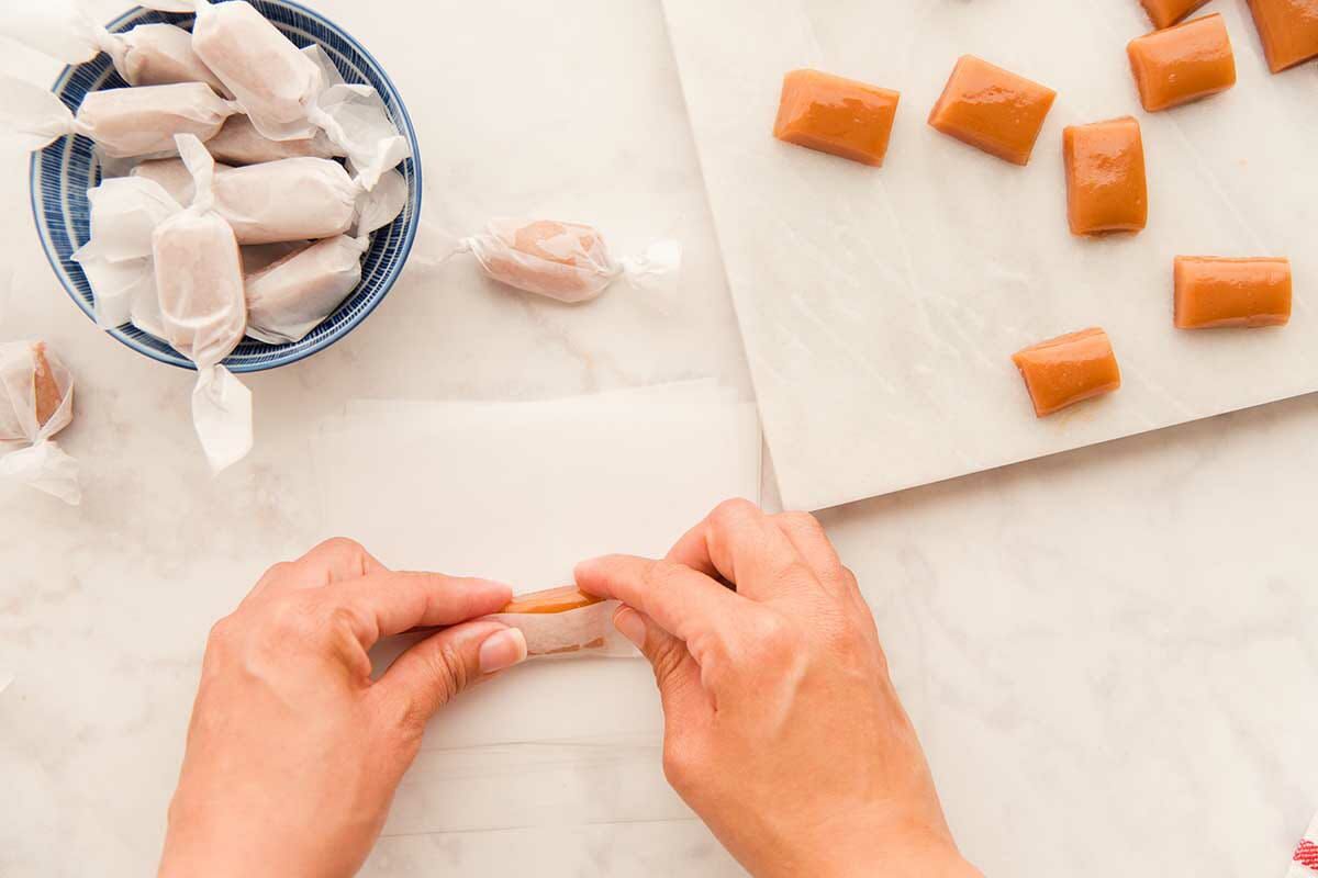 A person wrapping Caramel Candies in wax paper for a Soft Caramel Candy recipe.