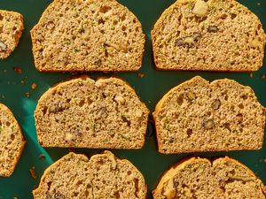 Slices of zucchini bread on a green surface with visible nuts and zucchini flecks
