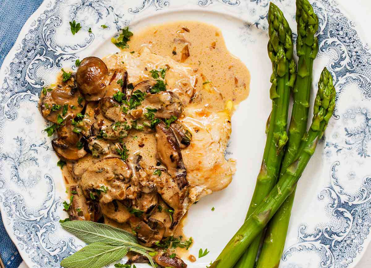 A beautiful decorated plate with a chicken breast, asparagus and creamy mushroom and sage sauce ready to eat