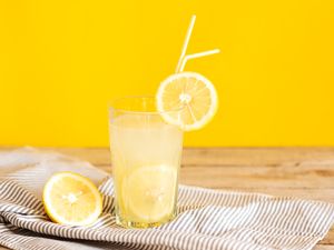 A glass of lemonade with lemon slices and straws on a striped cloth