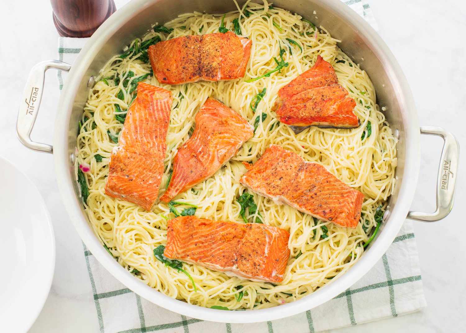 angel hair pasta in a sauce with arugula topped with salmon