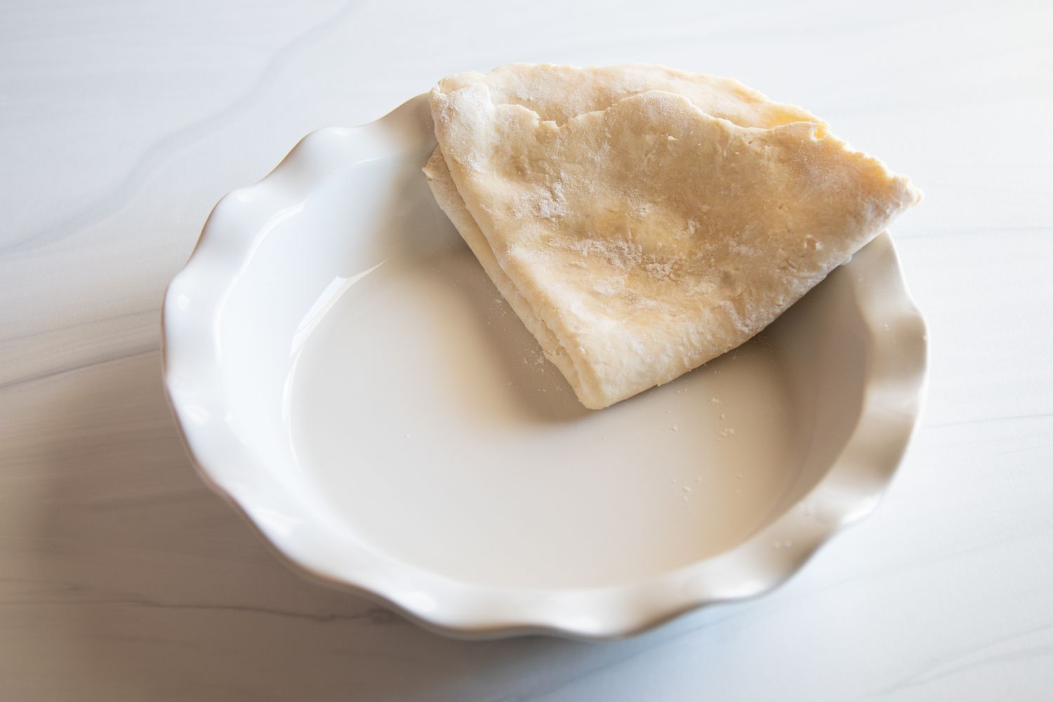 Folded pie dough in a ceramic pie dish to make Southern Peanut Pie.