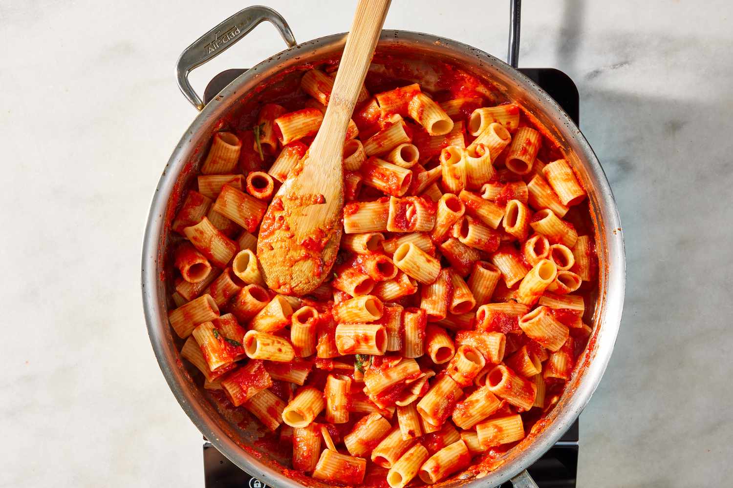 cooked rigatoni added to pot with tomato sauce for pasta alla norma recipe