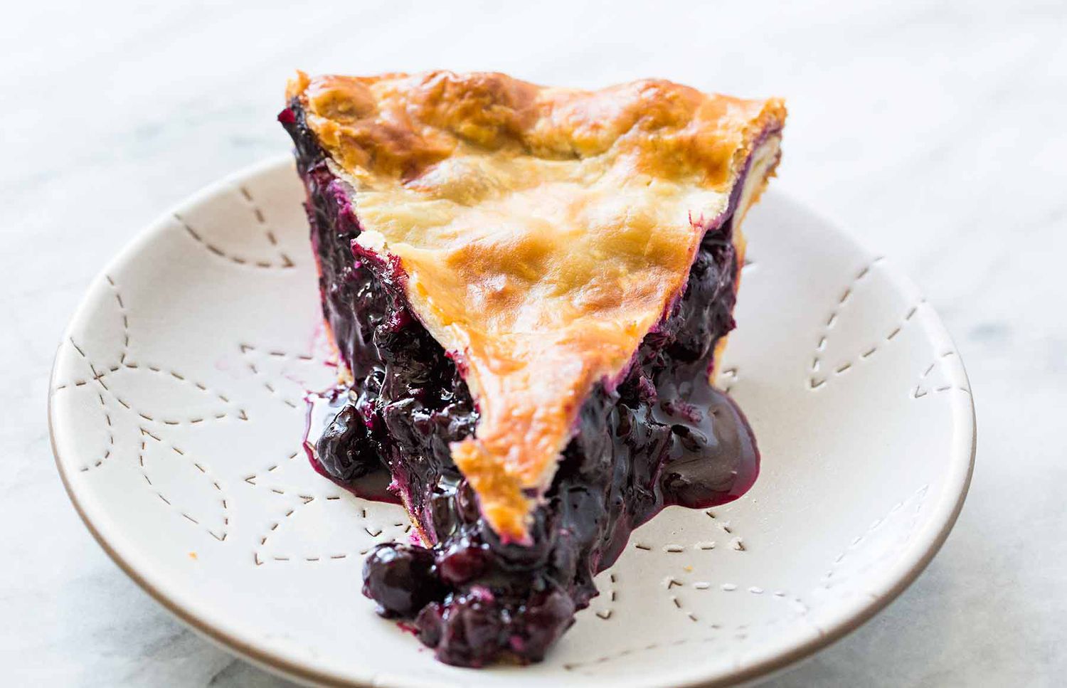 A slice of oozing, gooey blueberry pie with a golden brown crust