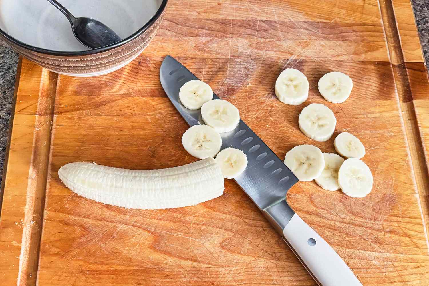 A sliced banana on a cutting board with a knife and a bowl nearby