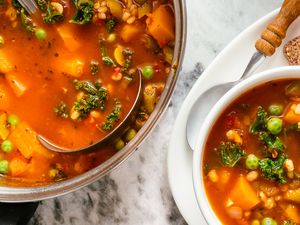A pot and a bowl of vegetable soup with a ladle bread on the plate beside the bowl