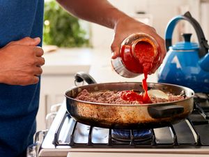 Person pouring tomato sauce into a skillet on a stove