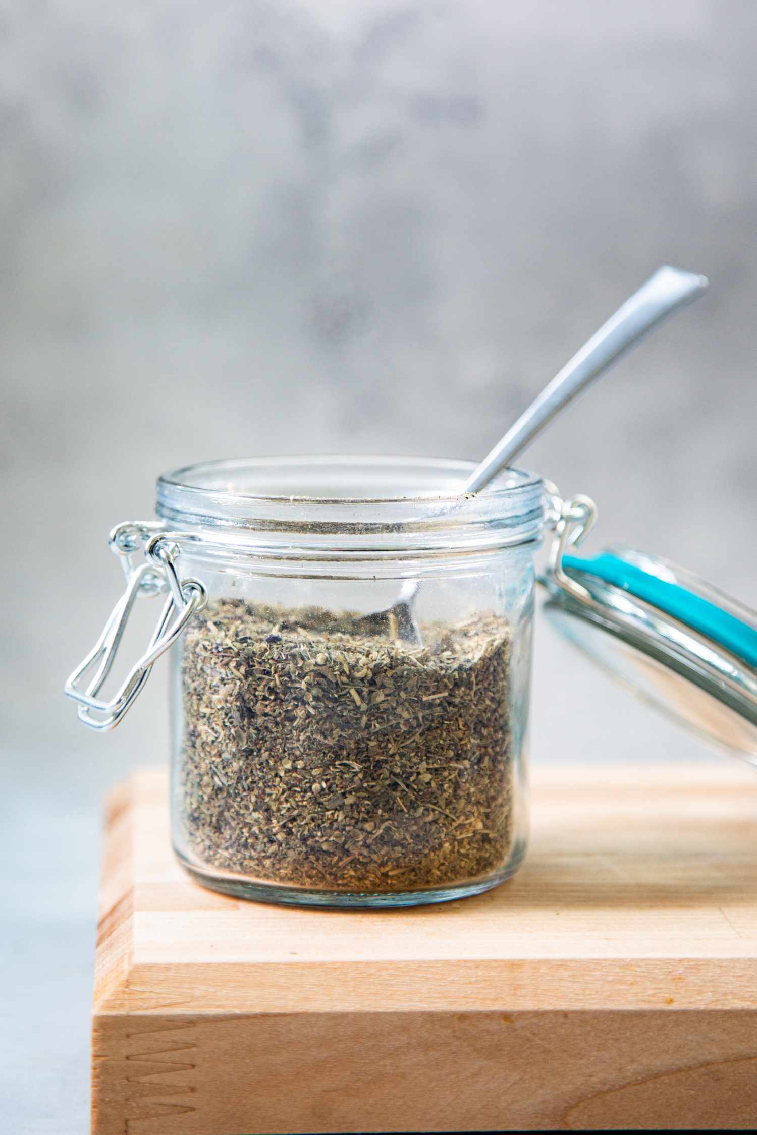 Italian Seasoning in a Jar with a Spoon, Sitting on a Cutting Board