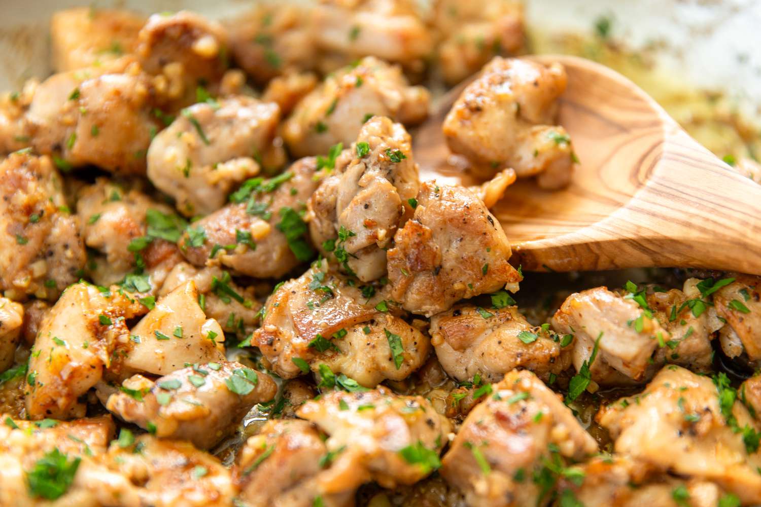Garlic butter chicken bites on a skillet with a wooden spoon