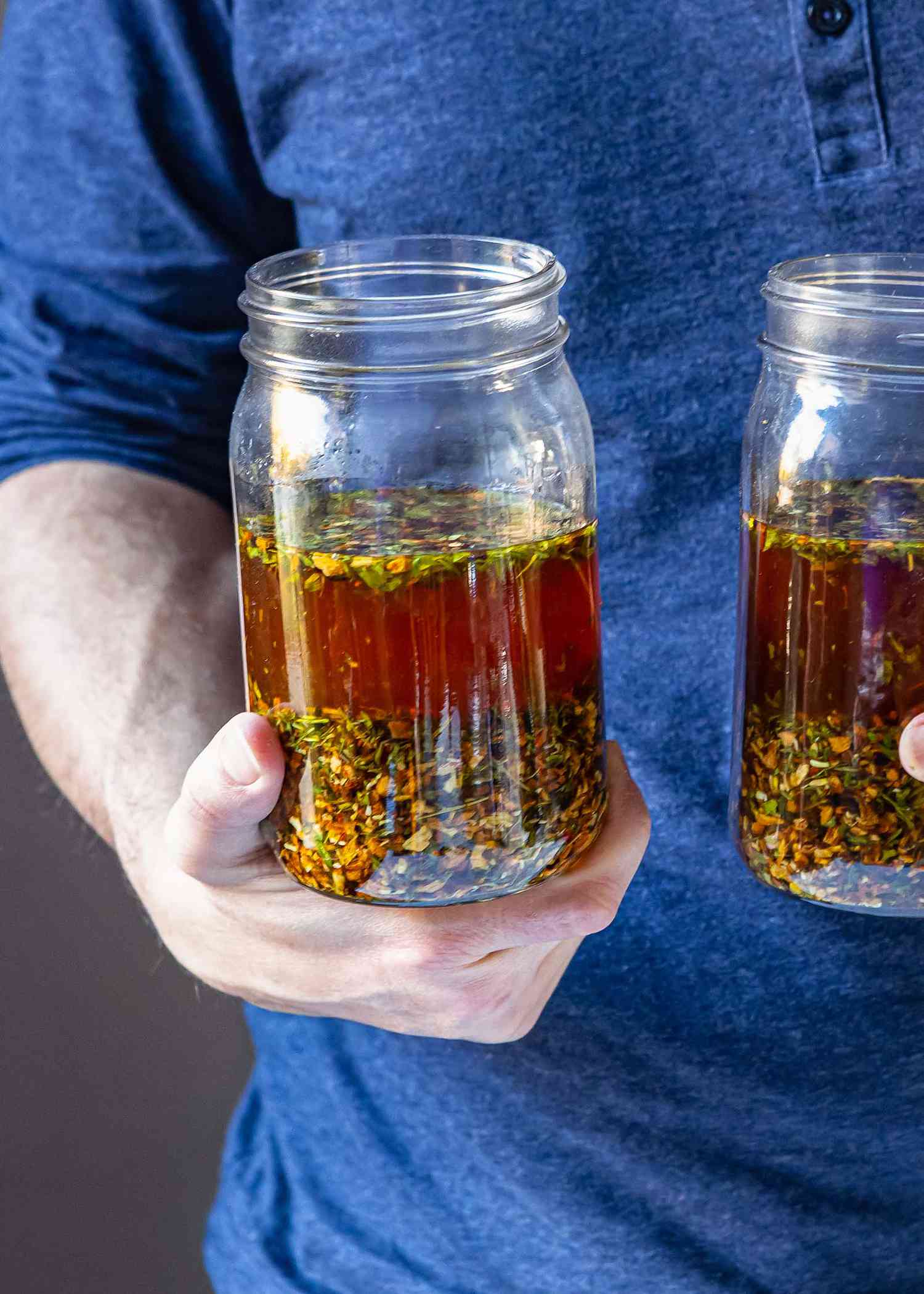 A person holding two glass jars with homemade campari inside.
