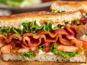 Closeup of a BLT sandwich with bacon, lettuce, tomato, and mayonnaise, on toasted bread slices, prepared and presented on a wooden surface