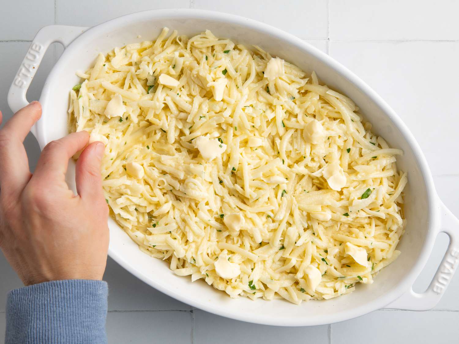 fingers putting butter on the top of shredded potato gratin