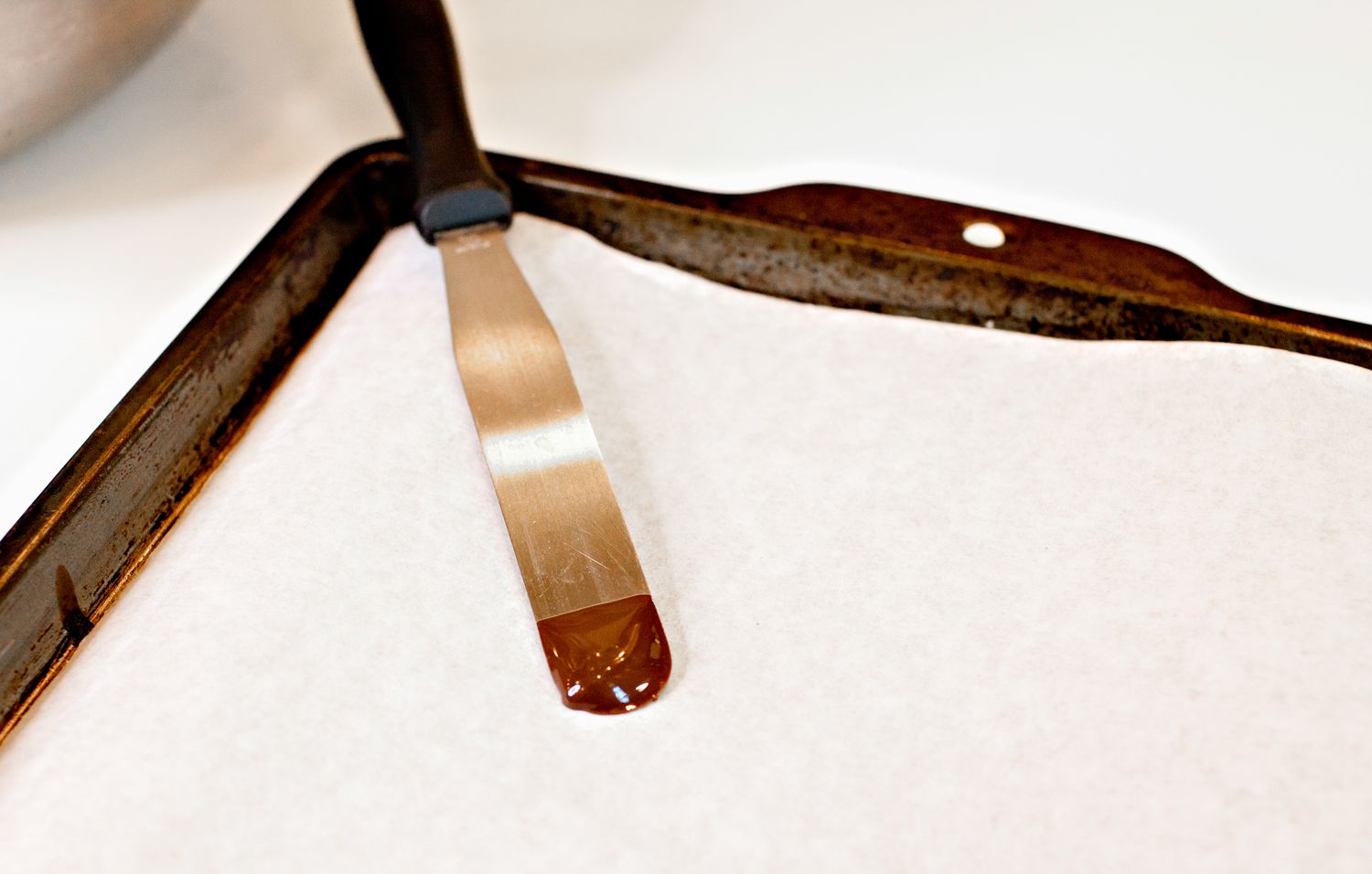 Chocolate on a Metal Icing Spatula Leaning Against a Parchment Paper Lined Baking Pan to Test for Temper 