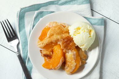 Peach cobbler served on a plate with a scoop of ice cream accompanied by a fork