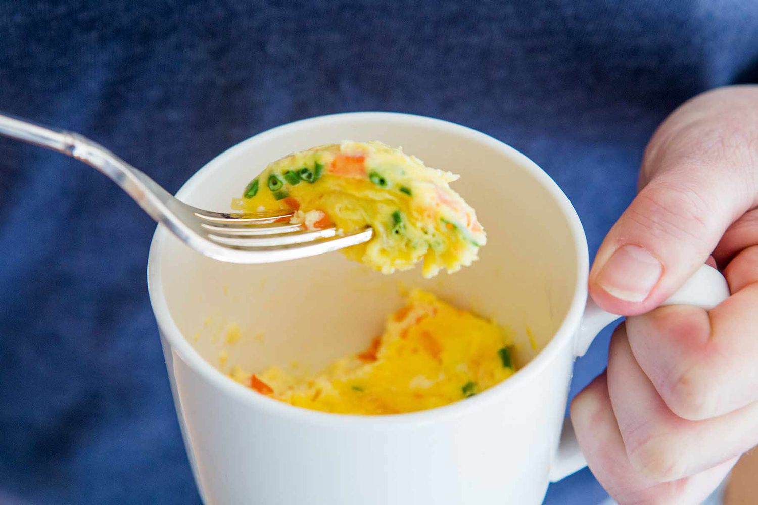 Person holding a mug with an omelette inside.