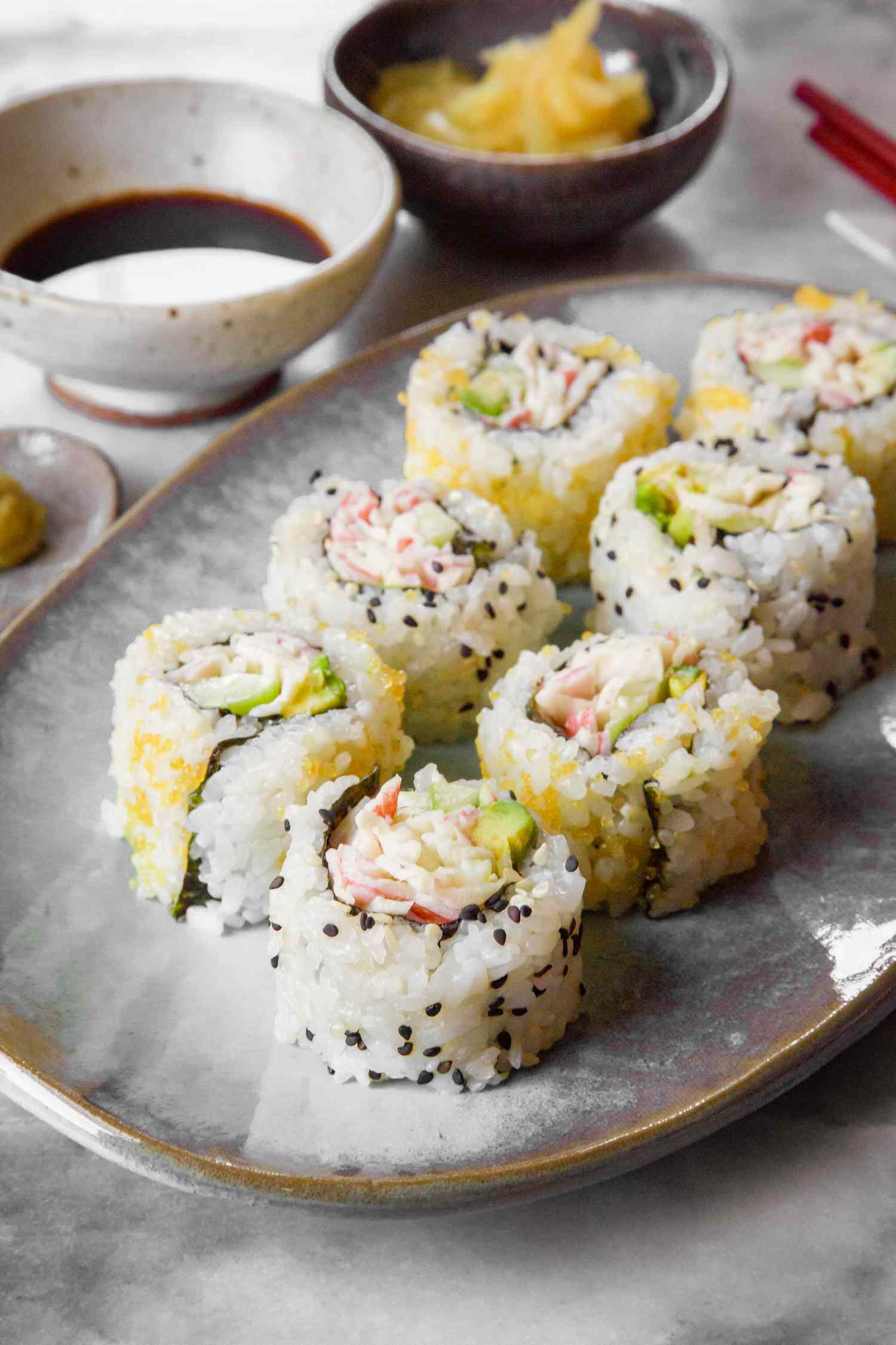 California Rolls on a Plate Next to a Small Bowl of Soy Sauce, Small Bowl of Pickled Ginger, and Small Saucer of Wasabi