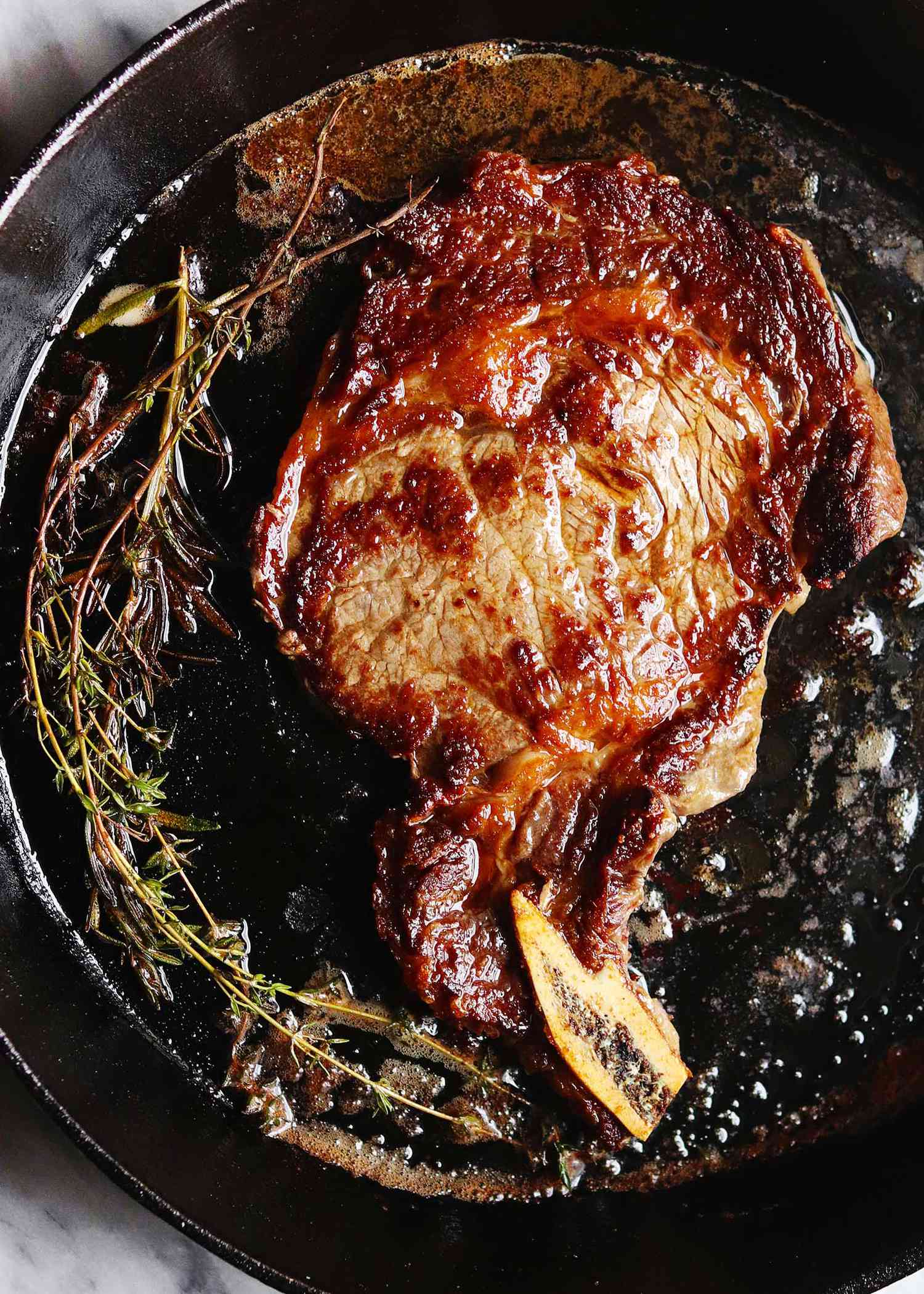 Bone-in steak in a cast iron skillet with sprigs of rosemary on the side.