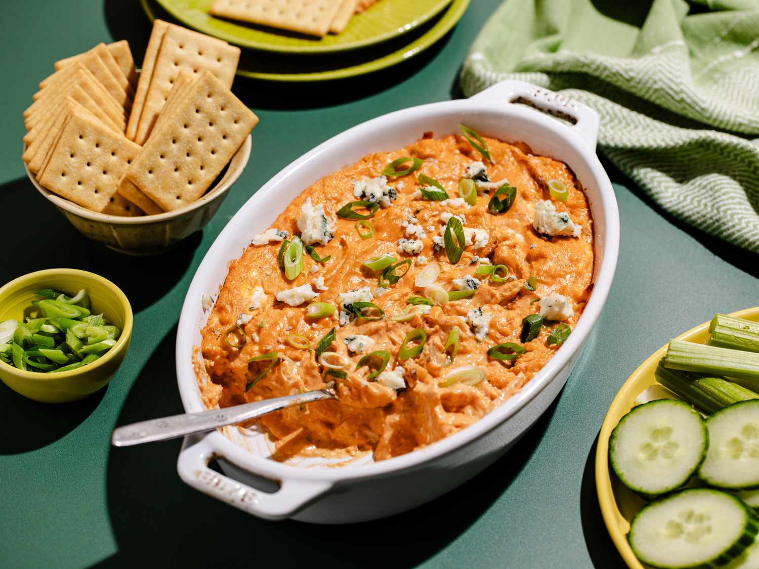 A casserole dish filled with chicken dip next to a bowl filled with crackers. 