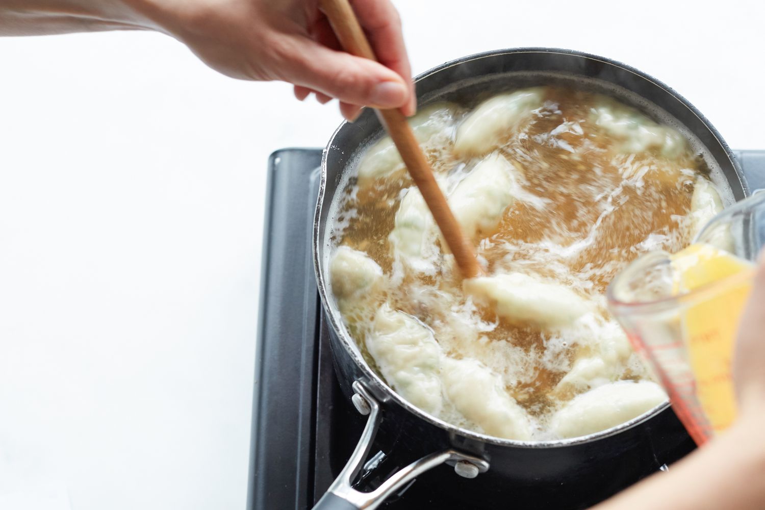 Drizzling in whisked eggs to a Korean dumpling beef soup in a pot on the stove.