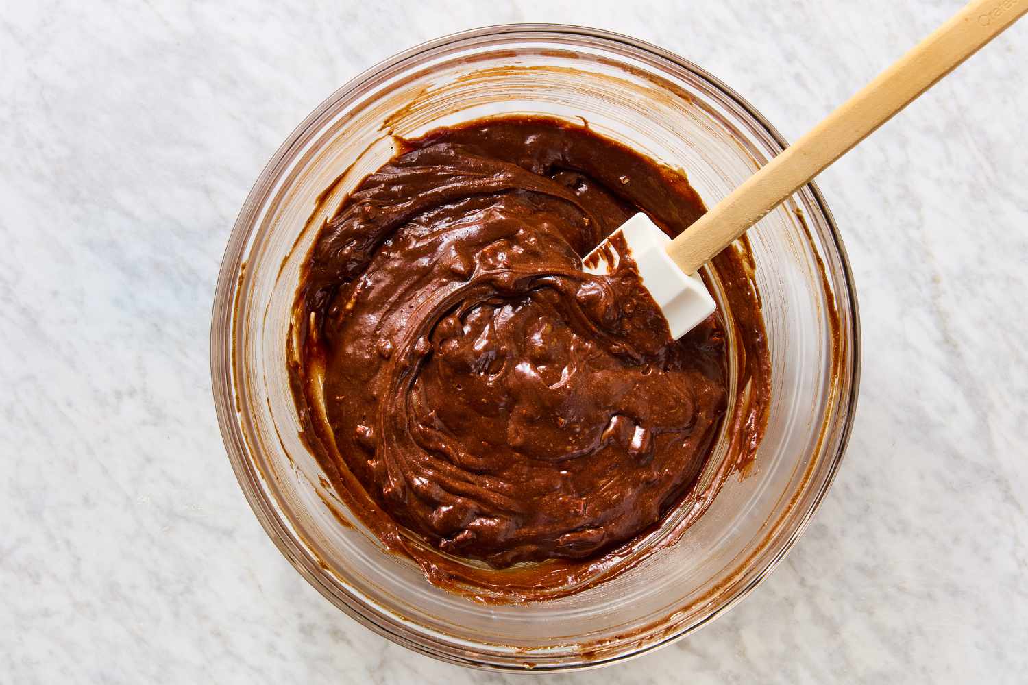 Overhead view of a clear glass bowl of the brownie batter mixture and a spatula for Mississippi Mud Pie recipe