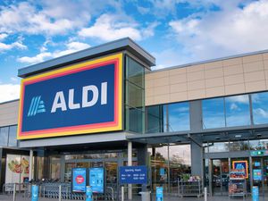 The exterior entrance of an Aldi supermarket with signage and glass windows, located under a bright sky