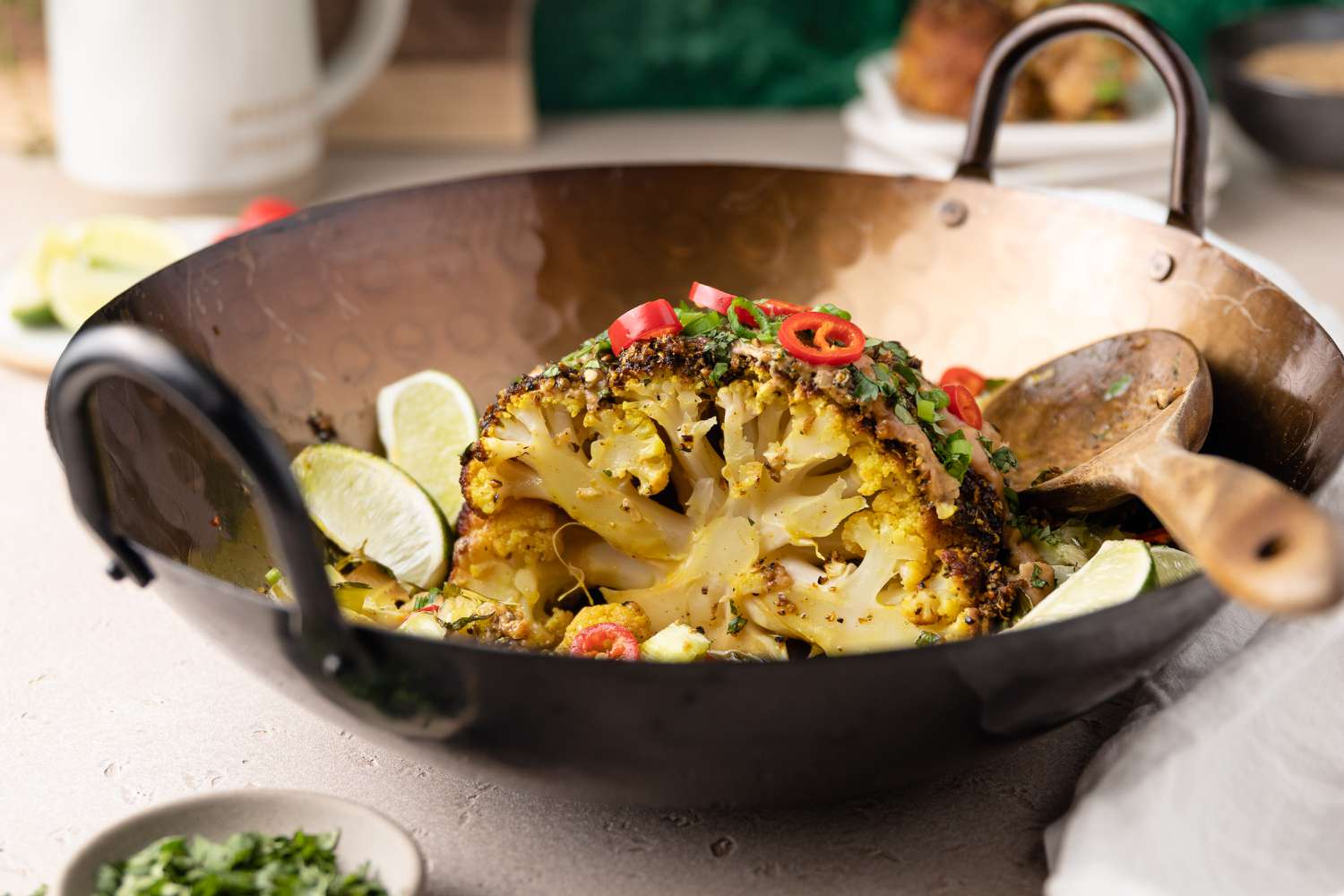 Head of Smoked Cauliflower Cut in Half in a Pan Garnished with Lime Wedges and Peppers for Smoked Whole Cauliflower with Spiced Soy Butter and Satay Sauce. 