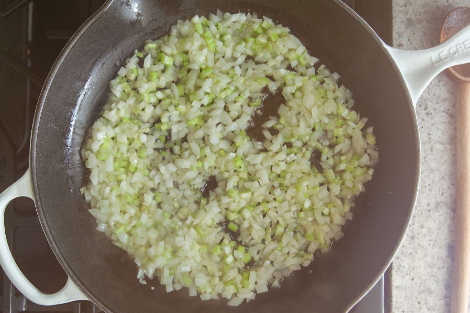 Overhead view of a cast iron skillet on a gas stove after adding onions and celery for Easy Porcupine Meatballs recipe