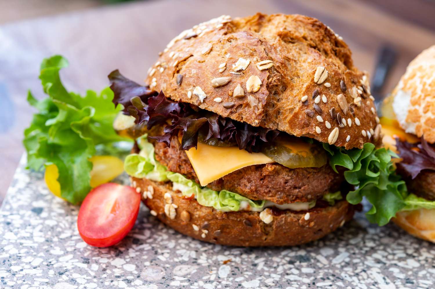 A whole grain bun sandwich with lettuce, cheese, and a patty on a surface